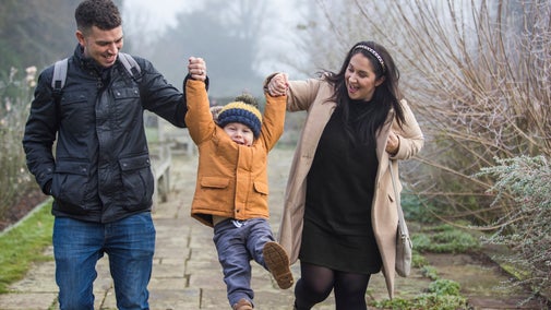 Two adults swing a child between them while walking along a garden path at Hinton Ampner in winter.